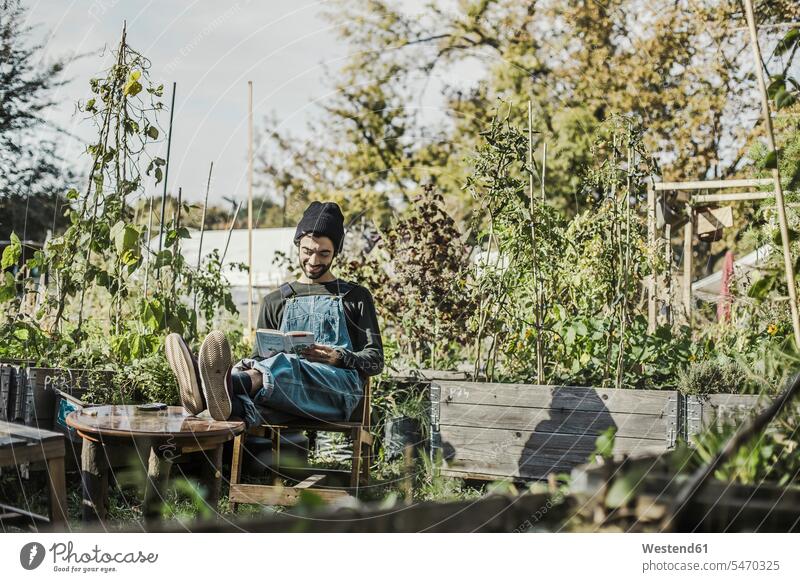 Lächelnder Mann, der ein Buch im städtischen Garten liest Bücher Urban Urbanität Urbanitaet Gärten Gaerten Männer männlich lächeln lesen Lektüre