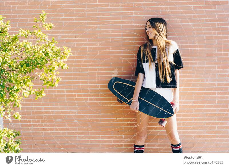Spanien, jugendliches Mädchen hält Skateboard an einer Ziegelmauer halten lächeln Backsteinwand Backsteinmauern Rollbretter Skateboards glücklich Glück
