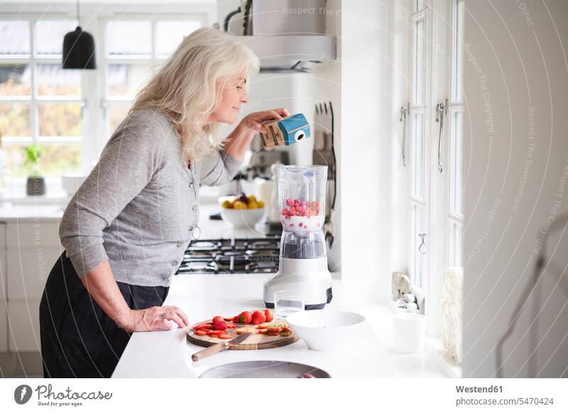 Ältere Frau gießt Milch in Prozessor bei der Vorbereitung Erdbeer-Smoothie in der Küche Farbaufnahme Farbe Farbfoto Farbphoto Dänemark Skandinavien