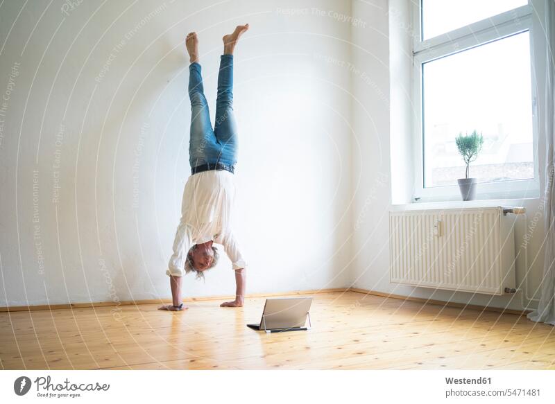 Ein reifer Mann macht einen Handstand auf dem Boden in einem leeren Raum und betrachtet eine Tablette Zimmer Räume Männer männlich Böden Boeden Tablet Computer