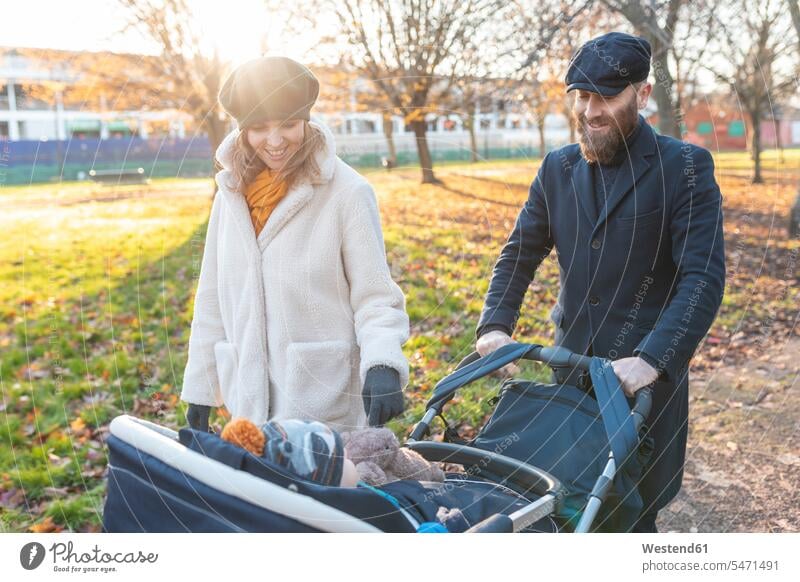 Glückliches Paar mit kleinem Sohn in einem Kinderwagen im Park Jacken Mützen freuen Frohsinn Fröhlichkeit Heiterkeit geniessen Genuss glücklich sein