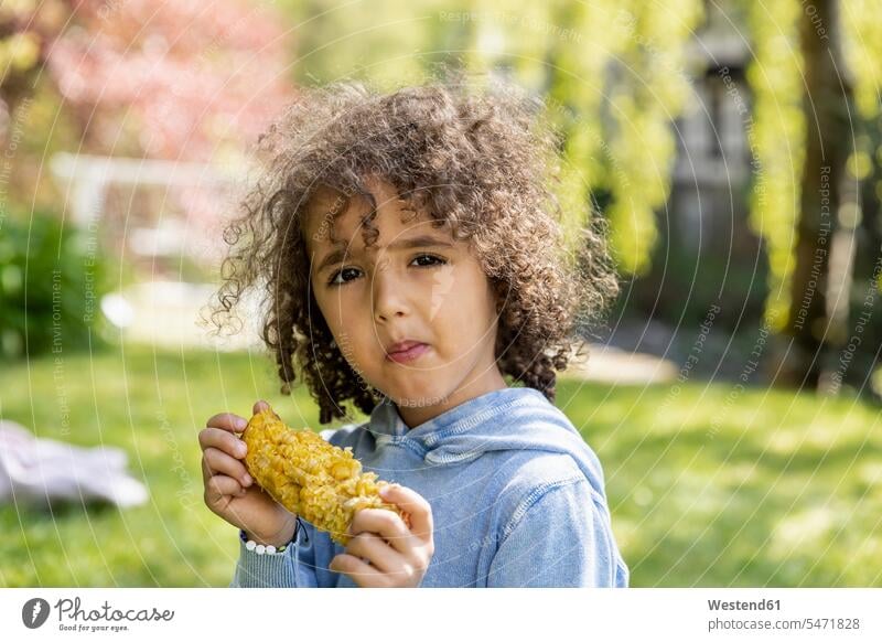 Porträt eines Jungen, der im Garten einen Maiskolben isst Leute Menschen People Person Personen gelockt gelockte Haare gelocktes Haar lockig lockiges Haar