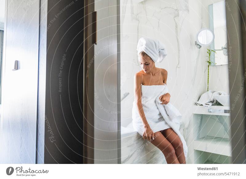 Frau in Handtücher gehüllt, auf dem Rand einer Badewanne sitzend In ein Handtuch gewickelt weiblich Frauen Badewannen Turban sitzt Erwachsener erwachsen Mensch