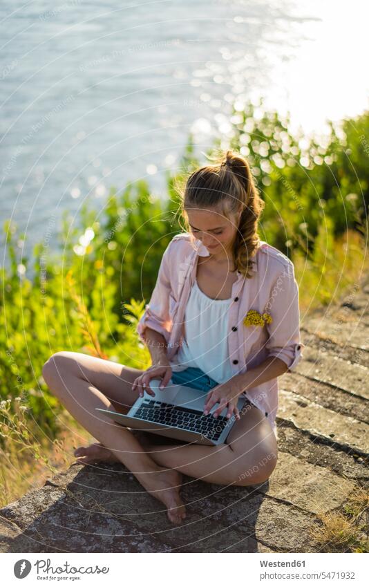 Frau sitzt am Flussufer im Sommer mit Laptop Notebook Laptops Notebooks Sommerzeit sommerlich Portrait Porträts Portraits sitzen sitzend Fluesse Fluß Flüsse