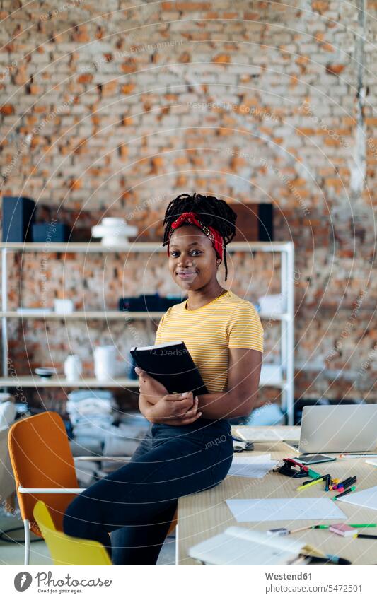 Porträt einer selbstbewussten jungen Frau am Tisch im Büro mit einem Notizbuch in der Hand Leute Menschen People Person Personen Afrikanisch