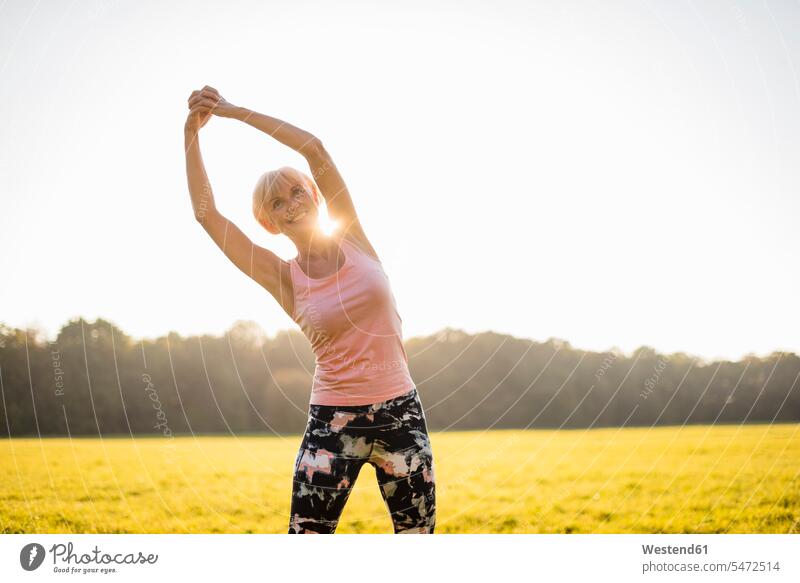 Senior Frau Stretching auf ländlichen Wiese bei Sonnenuntergang weiblich Frauen Wiesen Sonnenuntergänge dehnen strecken auf dem Land auf dem Lande Seniorin