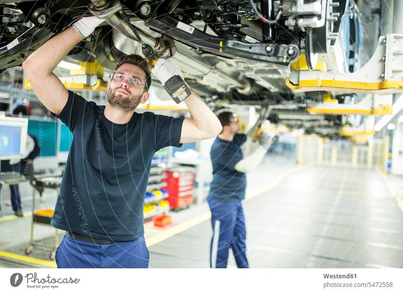 Zwei Kollegen arbeiten am Autounterboden in einer modernen Fabrik Arbeitskollege Arbeitskollegen Job Berufe Berufstätigkeit Beschäftigung Jobs Arbeiter T-Shirts