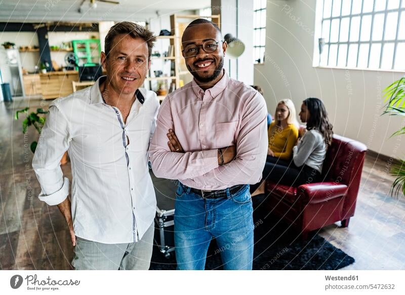 Porträt von zwei lächelnden Geschäftsleuten mit Mitarbeitern im Hintergrund im Loft-Büro Portrait Porträts Portraits Lofts Geschäftsmann Businessmann