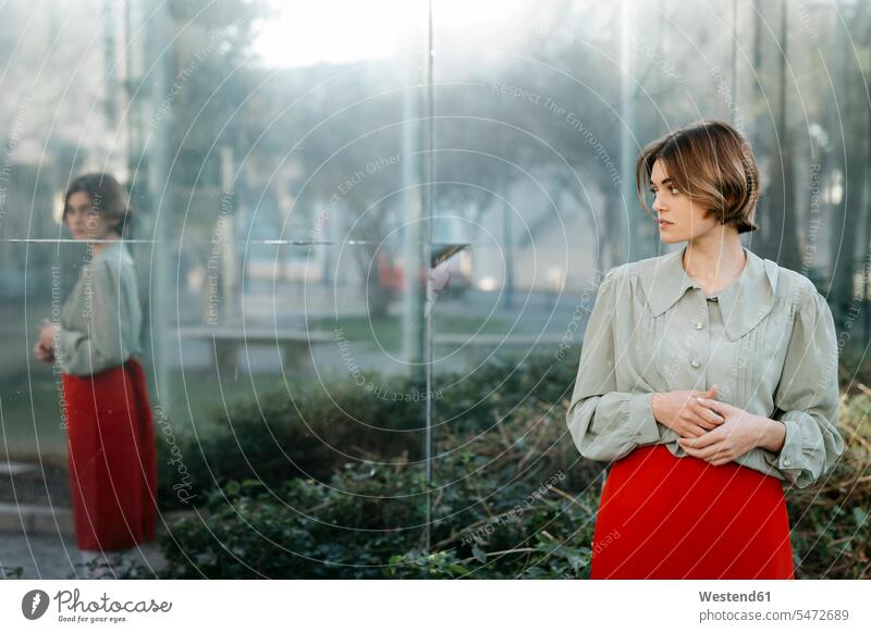 Porträt einer Frau in Vintage-Kleidung in einem städtischen Garten mit Spiegelung in der Glasscheibe Glasscheiben Roecke Röcke gefühlvoll Emotionen Empfindung