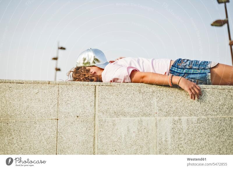 Mädchen an der Wand liegend, Basecap auf dem Kopf, verdecktes Gesicht Pause Pause machen Gesicht verdeckt Freizeit Muße Skateboarderin Skateboardfahrerin