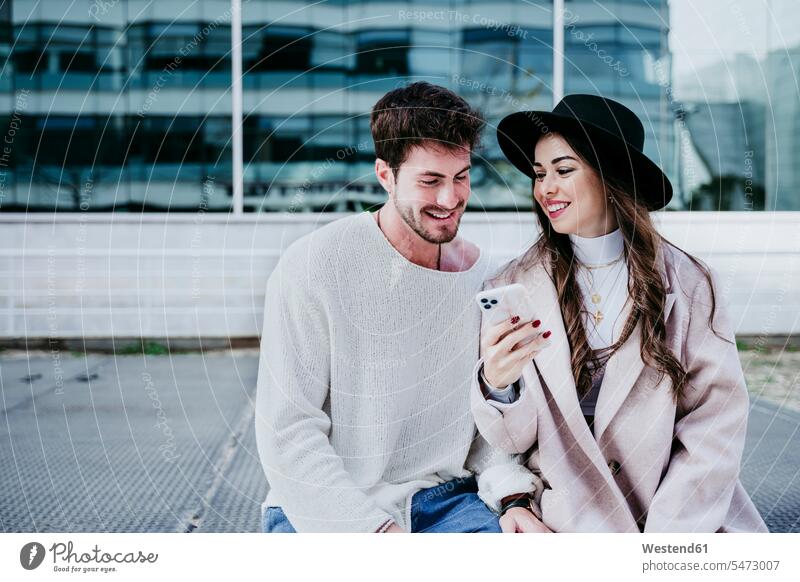 Lächelnde Frau zeigt dem männlichen Partner in der Stadt ein Smartphone Farbaufnahme Farbe Farbfoto Farbphoto Außenaufnahme außen draußen im Freien Tag