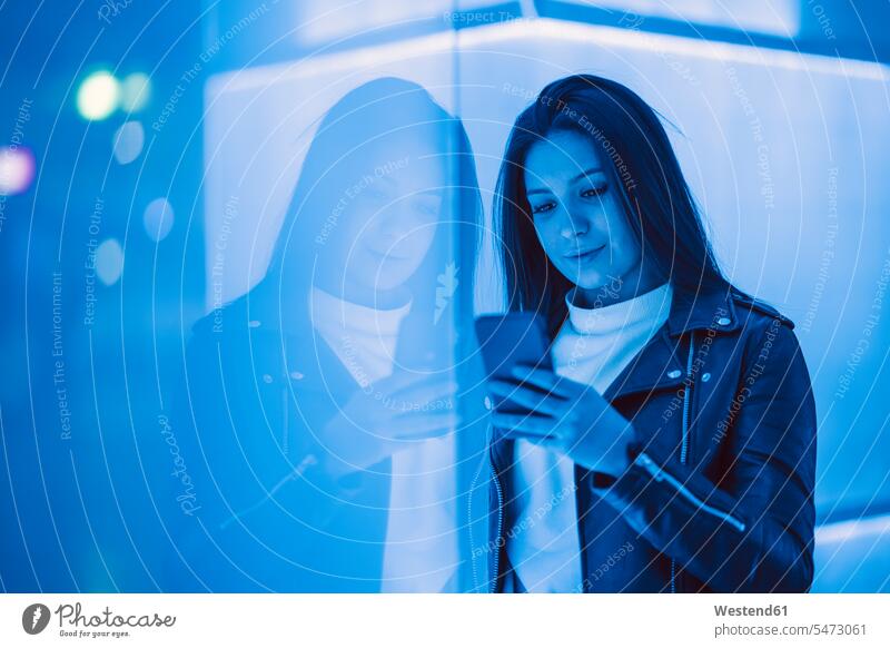 Porträt einer lächelnden Teenagerin in Lederjacke, die nachts auf ein Smartphone schaut Leute Menschen People Person Personen Europäisch Kaukasier kaukasisch 1