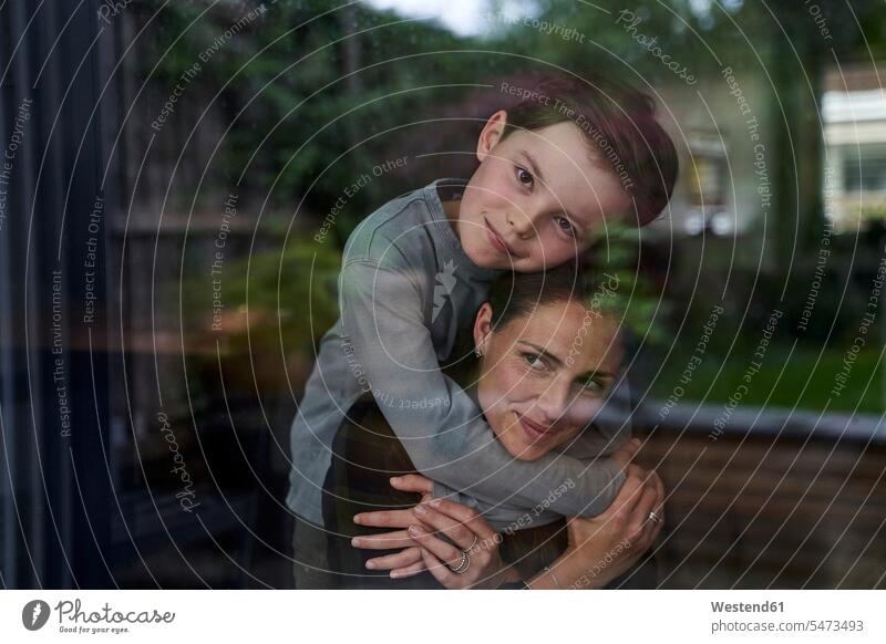 Liebender Sohn umarmt Mutter, während er zu Hause durchs Fenster gesehen steht Farbaufnahme Farbe Farbfoto Farbphoto Deutschland Freizeitbeschäftigung Muße Zeit