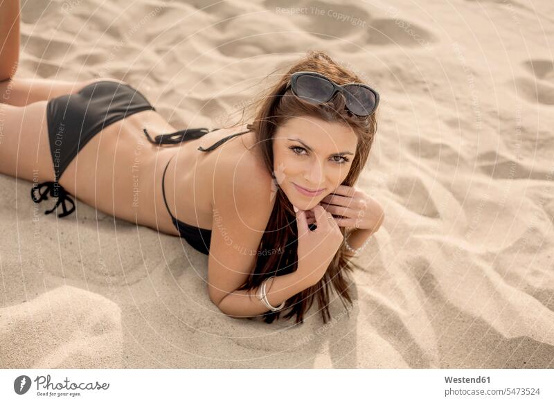 Schöne junge Frau liegt am Strand im Sand Farbaufnahme Farbe Farbfoto Farbphoto Außenaufnahme außen draußen im Freien Tag Tageslichtaufnahme Tageslichtaufnahmen