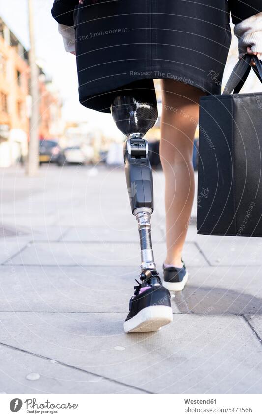 Niedriger Anteil einer Frau mit Beinprothese beim Gehen in der Stadt Taschen Jacken gehend geht Jahreszeiten Farben Farbtoene Farbton Farbtöne schwarze