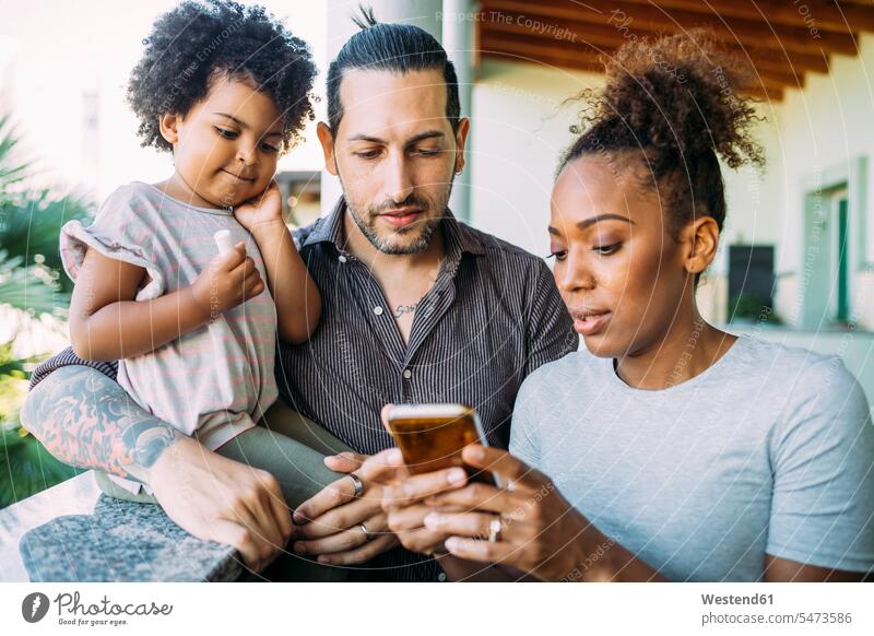 Frau zeigt Mann und Tochter ein Smartphone auf dem Balkon Farbaufnahme Farbe Farbfoto Farbphoto Freizeitbeschäftigung Muße Zeit Zeit haben Freizeitkleidung