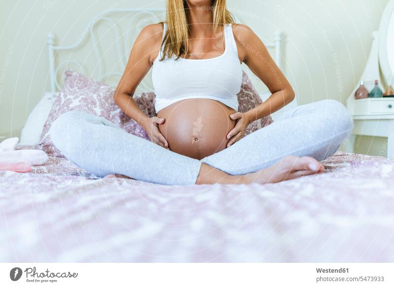 Nahaufnahme des Bauches einer schwangeren Frau, die auf dem Bett sitzt Betten Bäuche weiblich Frauen Schwangere schwangere Frau sitzen sitzend Oberkörper Torso