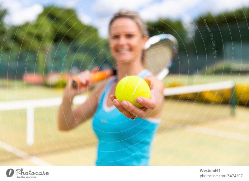 Lächelnde reife Frau hält einen Tennisball im Tennisclub Leute Menschen People Person Personen Europäisch Kaukasier kaukasisch 1 Ein ein Mensch nur eine Person