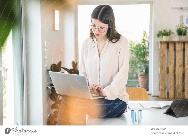 Junge Frau sitzt auf dem Tisch zu Hause mit Laptop sitzen sitzend Tische Notebook Laptops Notebooks weiblich Frauen Zuhause daheim Computer Rechner Erwachsener