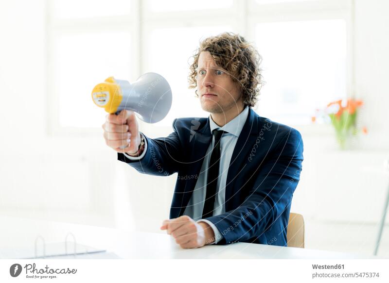 Geschäftsmann sitzt im Büro und probiert das Megaphon aus Businessmann Businessmänner Geschäftsmänner Office Büros versuchen Versuch sitzen sitzend erschrecken