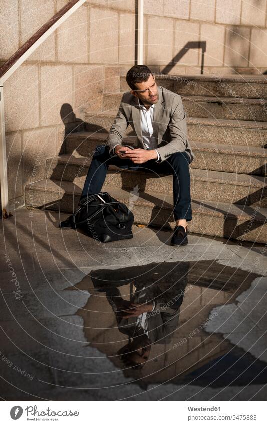 Geschäftsmann mit Tasche sitzt auf der Treppe mit Handy Businessmann Businessmänner Geschäftsmänner Taschen Mobiltelefon Handies Handys Mobiltelefone sitzen