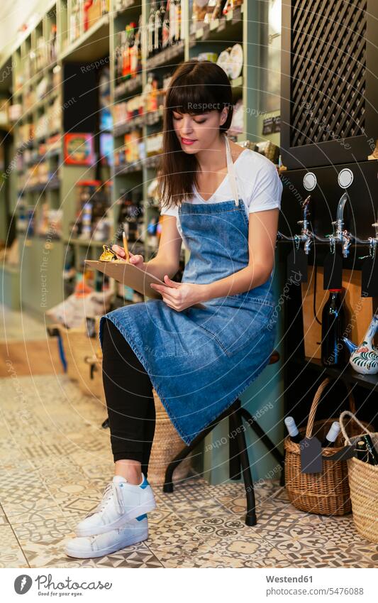 Frau sitzt in einem Geschäft auf einem Hocker und macht Notizen sitzen sitzend Shop Laden Läden Geschäfte Shops weiblich Frauen notieren Einzelhandel Handel