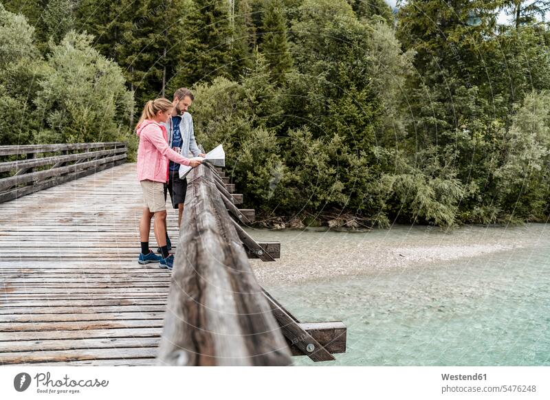 Junges Paar auf einer Wanderung beim Kartenlesen auf einer Holzbrücke, Vorderriss, Bayern, Deutschland Touristen Landkarten Jacken gehend geht Lektüre