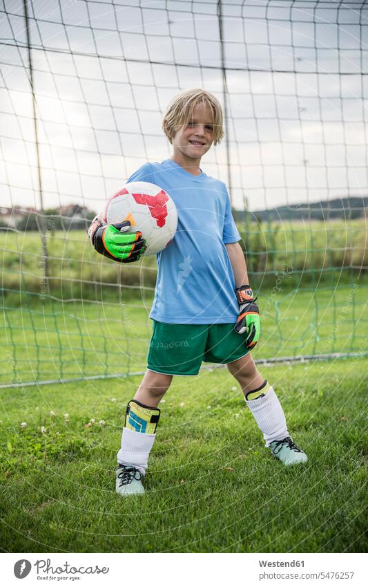 Porträt eines lächelnden jungen Fussballtorhüters, der den Ball auf dem Fussballplatz hält Torwart Tormänner Tormann Torwarte Tormaenner Portrait Porträts