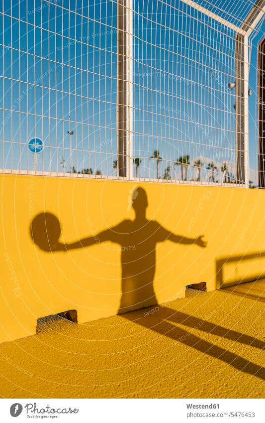 Schatten eines jungen Mannes, der Basketball auf gelber Wand im Sportplatz hält Farbaufnahme Farbe Farbfoto Farbphoto Spanien Freizeitbeschäftigung Muße Zeit
