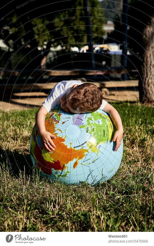 Junge umarmt Globus auf Grasland im Park bei Sonnenschein Farbaufnahme Farbe Farbfoto Farbphoto Spanien Freizeitbeschäftigung Muße Zeit Zeit haben