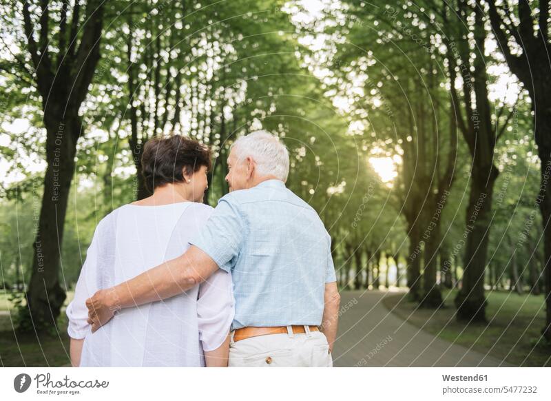 Rückenansicht eines älteren Paares, das in einem Park am Abend spazieren geht Partner Partnerschaften abends freuen Glück glücklich sein glücklichsein