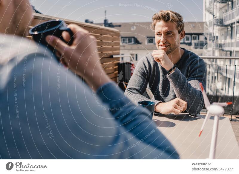 Zwei junge Männer sitzen auf dem Balkon, trinken Kaffee, machen ein Brainstorming sitzend sitzt Lösungen entwickeln Entwicklungen Innovationskraft innovativ