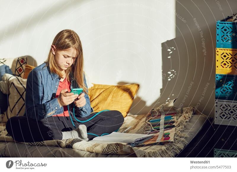 Mädchen sitzt zu Hause im Bett, macht Hausaufgaben und benutzt ein Smartphone Betten Stifte Telekommunikation telefonieren Handies Handys Mobiltelefon