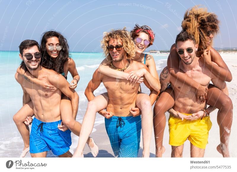 Freunde, die am Strand spazieren gehen und ihre Freundinnen Huckepack tragen Spaß Spass Späße spassig Spässe spaßig Beach Straende Strände Beaches Meer Meere