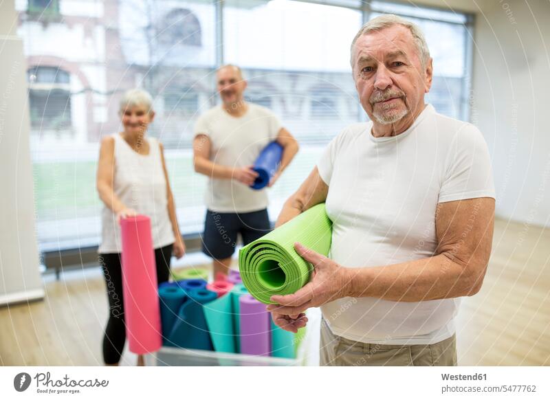 Glücklicher älterer Mann mit Yogamatte nach dem Unterricht glücklich sein glücklichsein stehend steht alte alter altes Pension pensioniert Pensionierung Rente