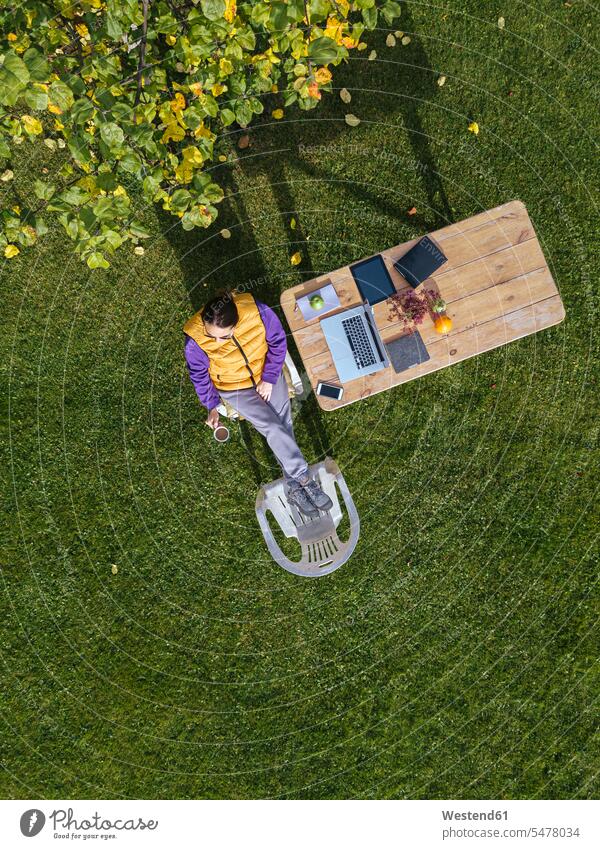 Frau trinkt Kaffee bei der Arbeit am Laptop im Garten Farbaufnahme Farbe Farbfoto Farbphoto Außenaufnahme außen draußen im Freien Tag Tageslichtaufnahme