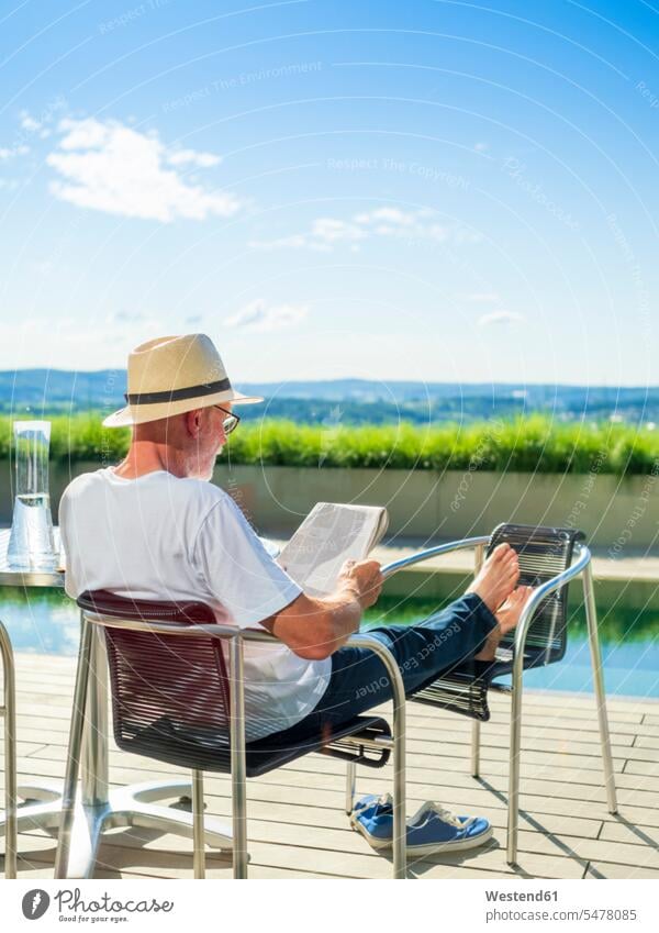 Rückansicht eines älteren Mannes, der Zeitungspapier liest und am Schwimmbad sitzt sitzen sitzend Stuhl Stuehle Stühle Zeitungen Urlaub Ferien Swimmingpool