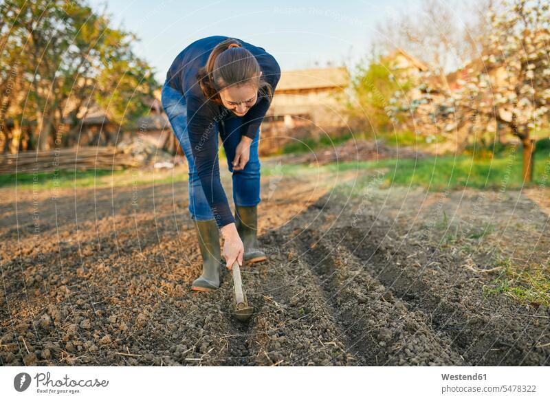 Frau in voller Länge mit Handpflug auf dem Boden bei der Gartenarbeit am Wochenende Außenaufnahme außen draußen im Freien Tag Tageslichtaufnahme