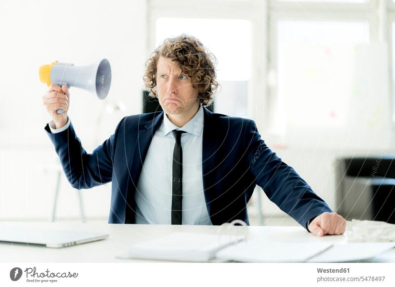 Geschäftsmann sitzt im Büro und probiert das Megaphon aus Megafon Megaphone Megafone Unzufriedenheit unzufrieden sitzen sitzend Businessmann Businessmänner