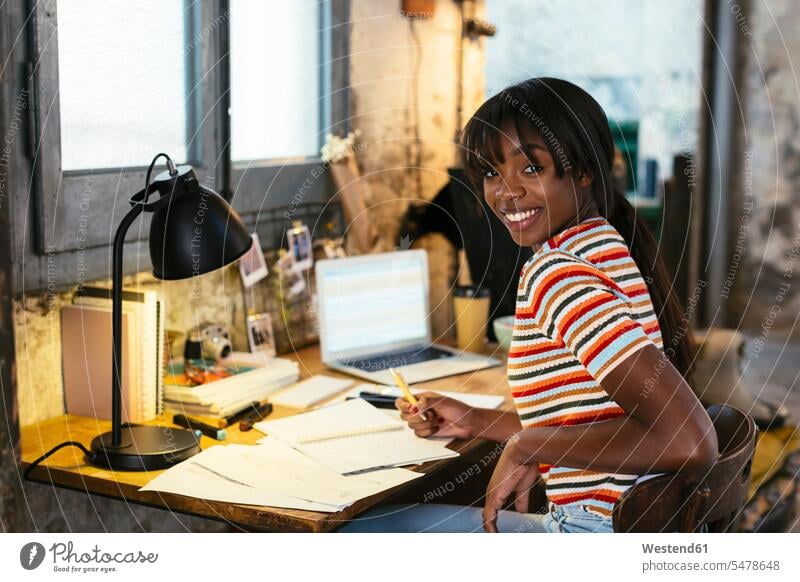 Porträt einer lachenden jungen Frau, die am Schreibtisch in einem Loft sitzt Arbeitstisch Schreibtische weiblich Frauen sitzen sitzend Portrait Porträts