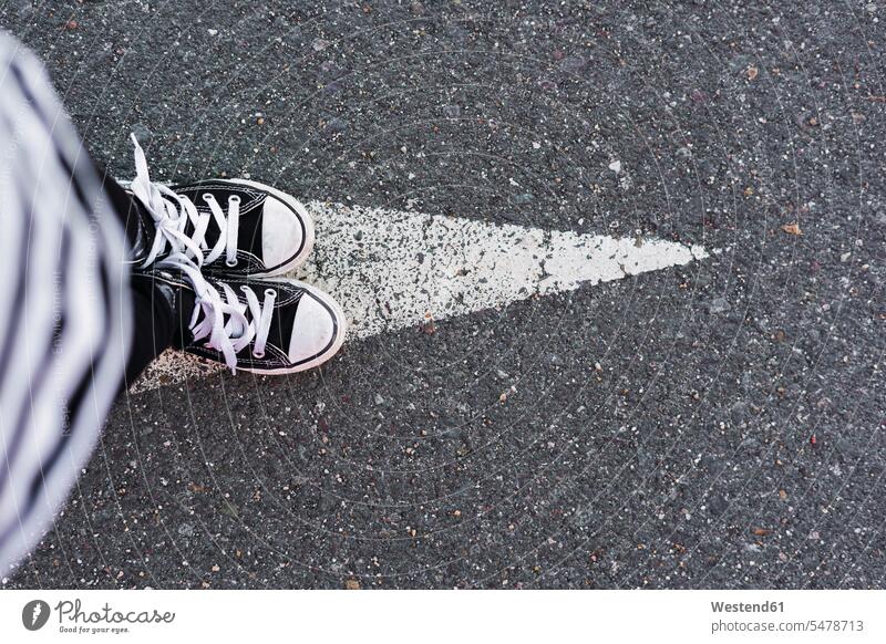 Mädchen in Turnschuhen steht auf Pfeil-Schild auf Fahrbahn, Ansicht von oben stehen stehend Perspektive Pfeilzeichen Pfeile weiblich eine Person single 1