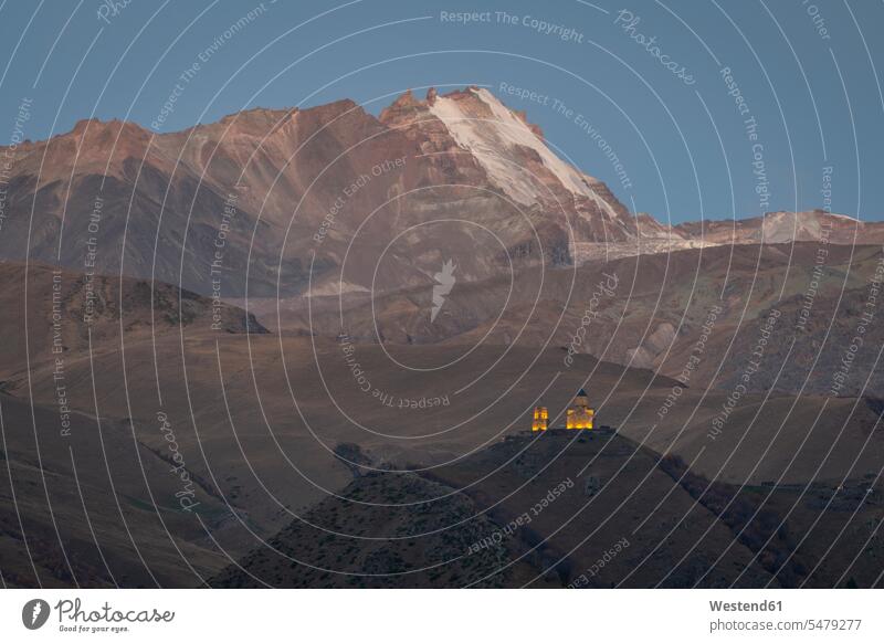 Georgien, Großer Kaukasus, Stepantsminda, Gergeti Dreifaltigkeitskirche Abend abends Abendlicht abendliches Licht verschneit schneebedeckt Christentum
