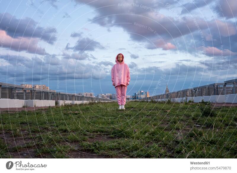 Bildnis einer jungen Frau mit rosa Haaren und rosa Kapuzenhemd auf Gras stehend Außenaufnahme außen draußen im Freien Kapuzenoberteil pinkfarbene Haare