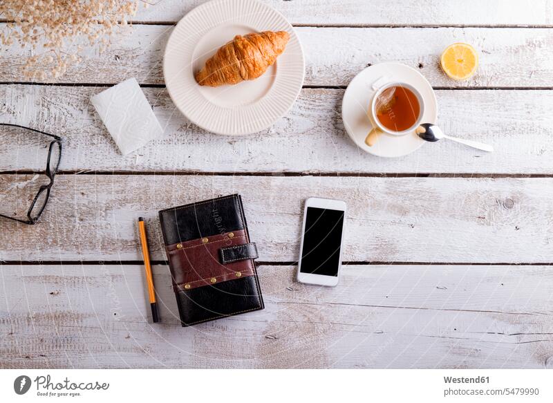 Tisch mit Croissant, Tee, Smartphone und persönlichem Organizer Tees Getränk Getraenk Getränke Getraenke Food and Drink Lebensmittel Essen und Trinken