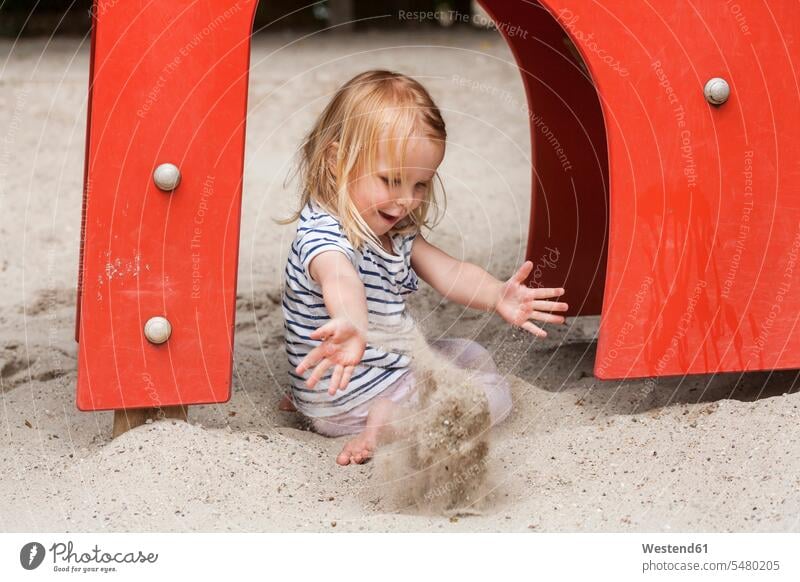 Blondes kleines Mädchen im Sandkasten auf dem Spielplatz weiblich Sandkästen Sandkiste Sandkisten Kind Kinder Kids Mensch Menschen Leute People Personen werfen