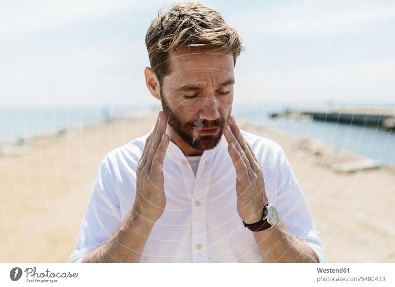 Mittelgroßer erwachsener Mann am Strand, der sein Gesicht berührt Männer männlich Portrait Porträts Portraits Beach Straende Strände Beaches müde abgespannt