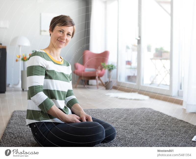 Porträt einer lächelnden Frau, die im Wohnzimmer auf dem Boden sitzt Portrait Porträts Portraits Wohnraum Wohnung Wohnen Wohnräume Wohnungen weiblich Frauen