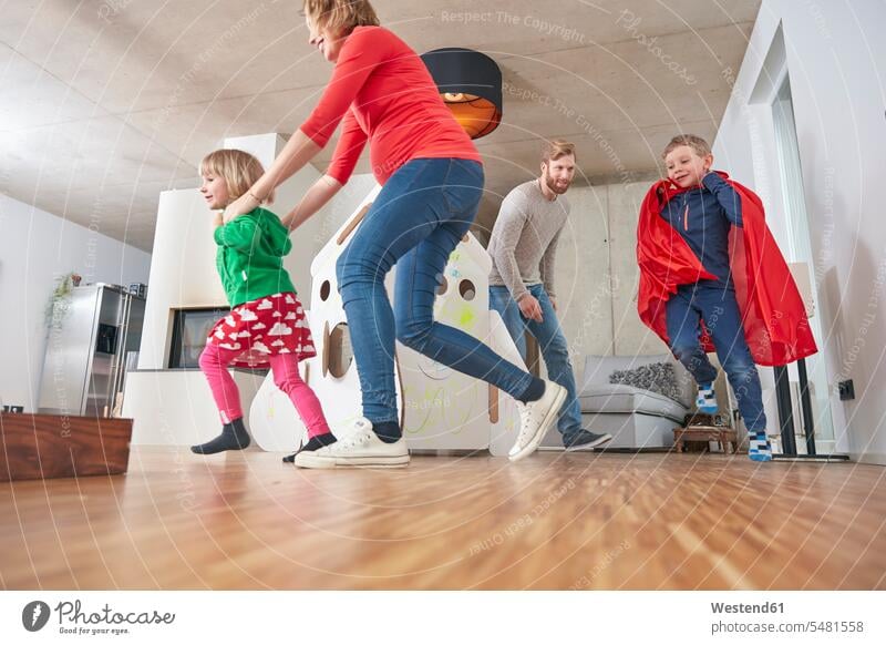 Glückliche Familie läuft im Wohnzimmer Deutschland Mann mittleren Alters Männer mittleren Alters junge Frau junge Frauen Junge Buben Knabe Jungen Knaben