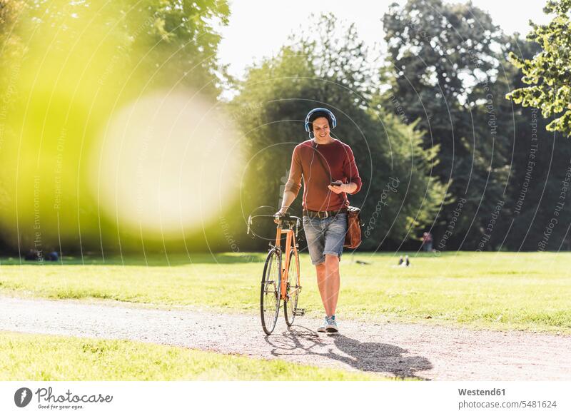 Mann mit Rennrad, der in einem Park mit Kopfhörern Musik hört Männer männlich Parkanlagen Parks Erwachsener erwachsen Mensch Menschen Leute People Personen