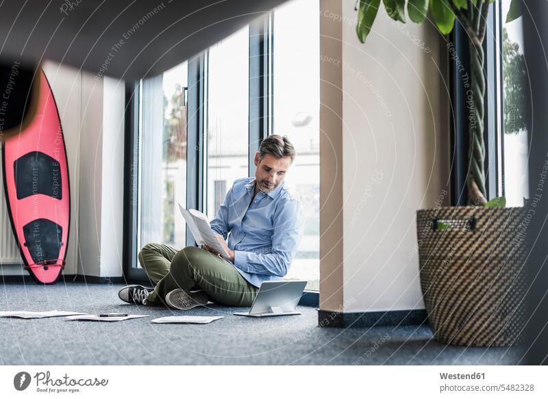 Geschäftsmann, der im Büro auf dem Boden arbeitet und sein Surfbrett an die Wand lehnt lesen Lektüre Tablet Tablet Computer Tablet-PC Tablet PC iPad
